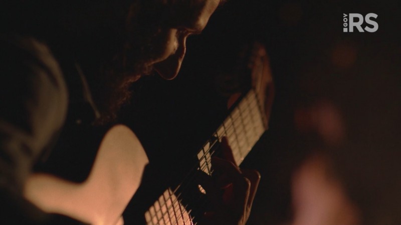 Homem tradicionalista tocando violão numa paisagem noturna com luz suave