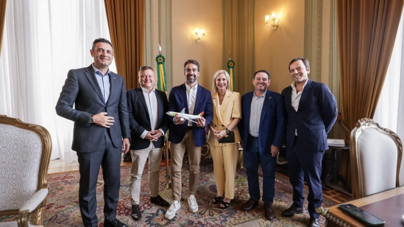 Foto do governador Eduardo Leite com comitiva da TAP. Todos est&atilde;o posando para foto. Governador segura uma miniatura de um avi&atilde;o.